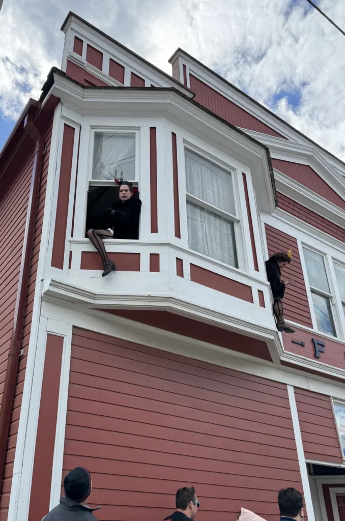View of women hanging out of 2nd story windows promoting The Days of ’98 Show dressed in the eras clothing.
