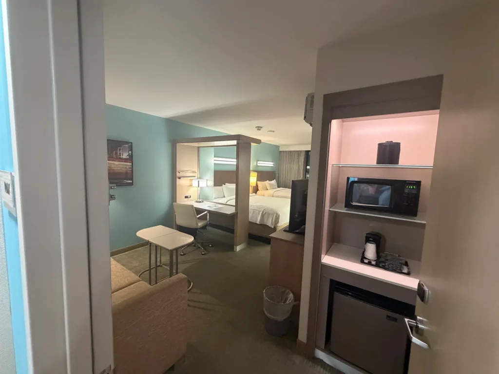 View from the doorway showing the sitting area, desk, two queen beds, microwave, and mini fridge