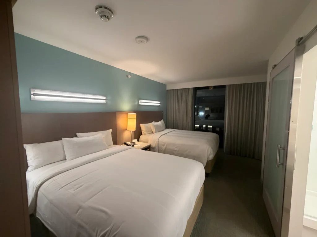 Two queen beds against a teal accent wall, with the sliding frosted glass bathroom door on the right